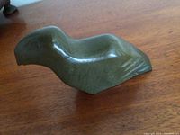 Side view of the green stone Inuit bird carving showing its smooth polished surface and wing details.
