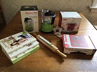 Overview photo showing all items on a wooden table including kitchen appliances in boxes, the rolling pin, cookie cutter, and cookbooks.
