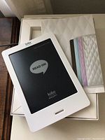 White Kobo eReader on white box with four colored quilted protective sleeves beside it.