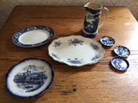 Wide photo showing full set of blue and white china pieces arranged on table, including plates, platter, small dishes, and pitcher