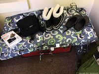 Lot of winter clothing and accessories arranged on patterned fabric, showing Sorel boots, Crocs, backpack, and traction device box