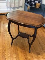 Side view of the vintage hardwood side table showing curved legs and scalloped edge top.