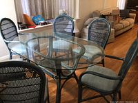 View of oval glass top table with six dark wicker chairs showing cushioned seats and wicker backs.