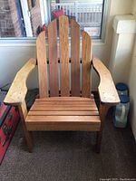Front view of one wooden Muskoka chair showing the slatted back with five vertical curved panels and wide armrests, wood worn and weathered.