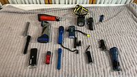 Photo showing 14 flashlights arranged on a beige blanket, sizes range from small to large with various colors and styles including a Coleman Husky flashlight.
