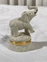 Front side view of white porcelain elephant trinket box with raised trunk and gold accents, hinged lid visible at base.