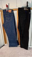 Two pairs of jeans hanging next to each other, one blue Levi's and one black Wrangler