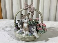 Front view of figurine showing three kittens and flowers inside basket, with braided handle topped by a bow.