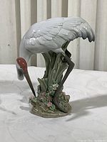 Porcelain crane figurine bending forward with detailed feathers and floral base, showing red head and dark legs.