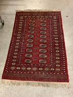 Full view of the small red area rug laid out flat, displaying overall pattern with rows of medallions and borders