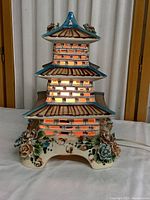 Front view of vintage ceramic pagoda lamp lit from within showing brick patterned midsections and floral base decoration.