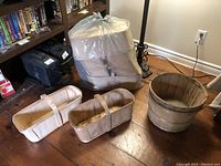 Photo showing two rectangular six quart baskets with handles and one round half bushel wooden basket on a wooden floor near furniture.