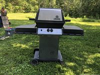 Full view of the Broil King BBQ grill on grass with side shelves and wheeled base.