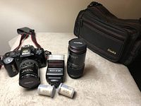 Full camera set arranged on surface showing Nikon F401 camera with attached 28-80mm lens, Black's AF 66N flash, 70-210mm telephoto lens, camera bag, two rolls of Kodak 400 ISO film, and strap.