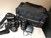 Photo of Minolta Maxxum 7000 camera with lens, external flash, camera strap, and carrying bag on a white surface