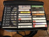 Photo showing a partially open black soft carrying case containing approximately 21 cassette tapes visible with various album titles and labels.