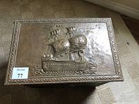 Top view of the stamped brass coal box lid displaying a detailed embossed three-masted ship on waves with decorative border.