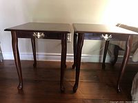 Front view of two matching wooden end tables with curved legs and brass handles on drawers.