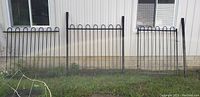 Black steel fence sections visible against the side of a building, includes two fence panels, a gate section, and posts.