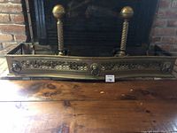 Full front view of the brass fireplace fender showing overall shape, framing, and lion head decorations.