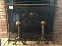 Full view of brass fireplace screen with mesh and pair of cast steel andirons with ball finials in front.