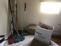 Cleaning tools grouped together in a corner: mops, broom, duster, Shark cleaning tool and boxes