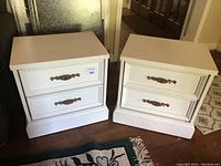 Photo showing two matching white painted two-drawer nightstands side by side on floor, with visible metal handles and base molding.