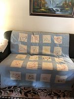 Blue quilt draped over a couch showing embroidered animal and bird motifs on cream squares against blue background.