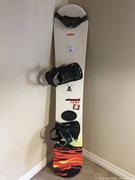 Full view of the white Oxygen Element 580 snowboard with black bindings attached and black goggles placed on the board.