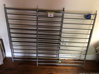 Two identical steel baby gates placed side by side on a wooden floor against a wall, showing the full width and locking mechanisms of both gates.