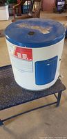 Full view of the 12 gallon electric water heater showing its white body, blue top, and blue side panel with a red and white label.