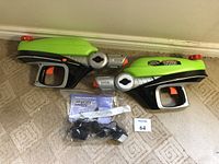 Two Water Warriors Tarantula motorized water sprayers side by side on carpet, with instruction manual and chargers below.