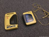 Two yellow Sony Sports Walkman cassette players and one set of yellow wired headphones on a carpeted floor