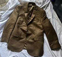 Rust-colored men's blazer laid flat on white fabric background. Shows full front and arm details.