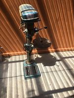 Front view of Busy Bee heavy duty floor standing drill press on concrete floor with a wood background. Shows motor housing, adjustable round work table, and base.