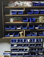 Wooden shelving filled with blue plastic bins holding assorted nails, nuts, bolts, and screws with some bins covered with bags.