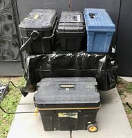 Four various sized used tool boxes placed on a concrete slab outdoors with a black gate background.