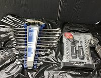 Photo showing Mastercraft 14-piece combination wrench set (2 pieces missing) on the left and Husky 46-piece stubby wrench and socket set on the right, all tools in plastic holders on black surface.
