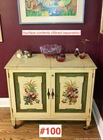 Front view of painted bar cabinet showing double doors with decorative fruit and wheat painted panels, brass hardware, and closed top flaps.