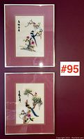 Pair of framed silk embroideries hung on a burgundy wall showing birds and floral designs with Chinese characters.
