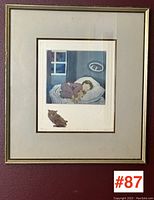 Framed signed print hanging on a wall with label #87 visible, showing the entire framed artwork.