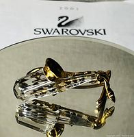 Close-up front view of miniature Swarovski saxophone on mirrored surface reflecting detailed facets and gold accents