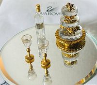 Full set of Swarovski crystal wedding cake, wine bottle and two wine glasses on reflective surface with Swarovski packaging in background.
