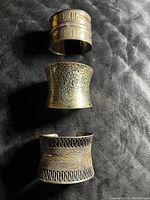 Three vintage Tibetan tribal style wide bronze tone cuff bracelets laid on black fabric showing different tribal patterns and details.