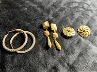 Full lot showing three pairs of earrings: large crystal encrusted gold tone hoops, vintage gold tone drop earrings with white and coral pink accents, and vintage gold tone swirl earrings.