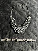 Photo showing the crystal cluster necklace and black onyx silver tone bracelet laid flat on black fabric background.