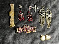 Full view of six vintage jewelry items on black fabric showing bracelet, two pairs of earrings, two pendants, and an additional gold-tone item with stones.