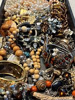 Photo showing assortment of vintage jewelry including necklaces, bracelets, brooches with faux pearls, wooden beads, rhinestones, and metal pieces.