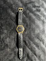 Full view of the Movado wristwatch with black leather strap and gold case on a black background