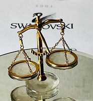 Front angled view of Swarovski crystal balance scales showing clear crystal base, gold arms and chains, and two round glass pans.